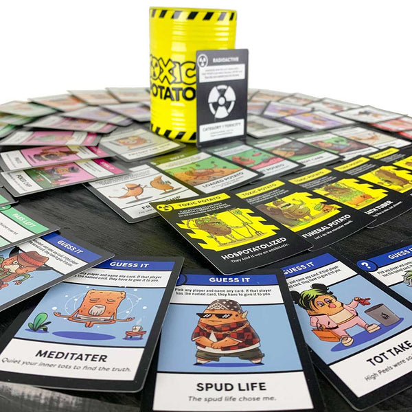 The Toxic Potato barrel packaging is in the center of a round table with all of the different Toxic Potato cards spread in a circle around the outside of it.